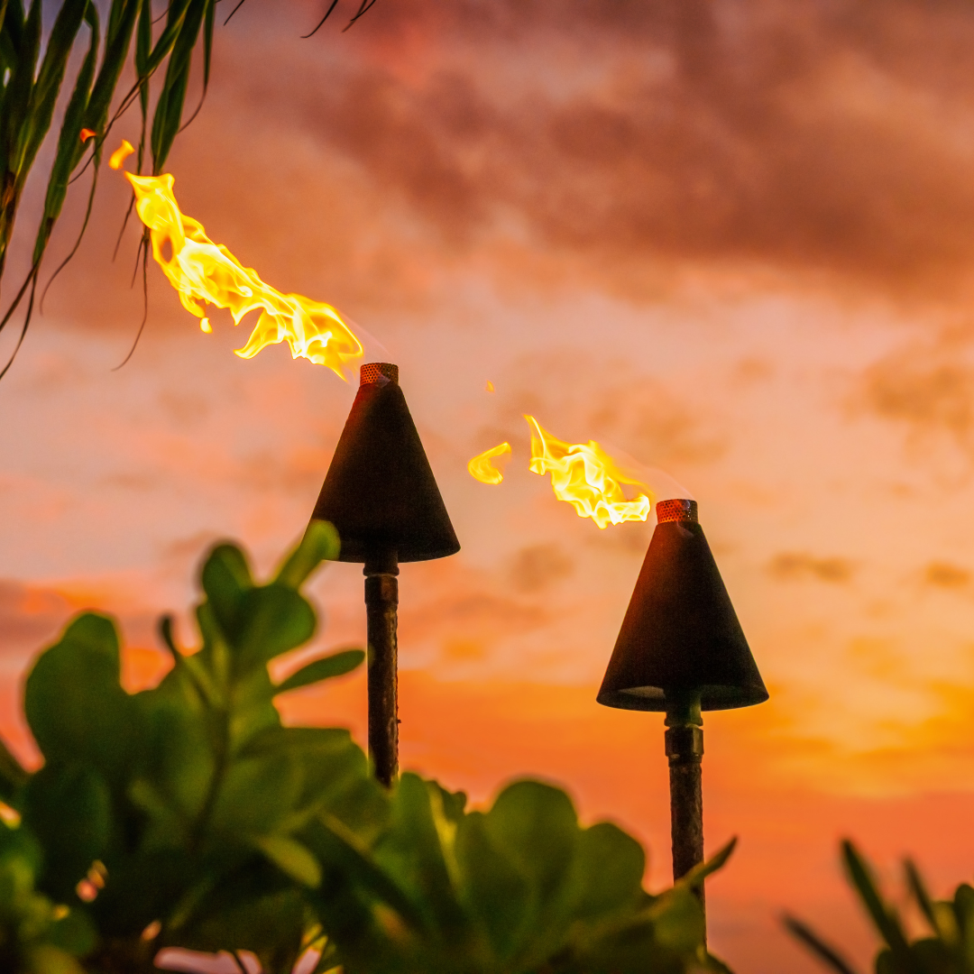 two lit tiki torches glow against a sunset background