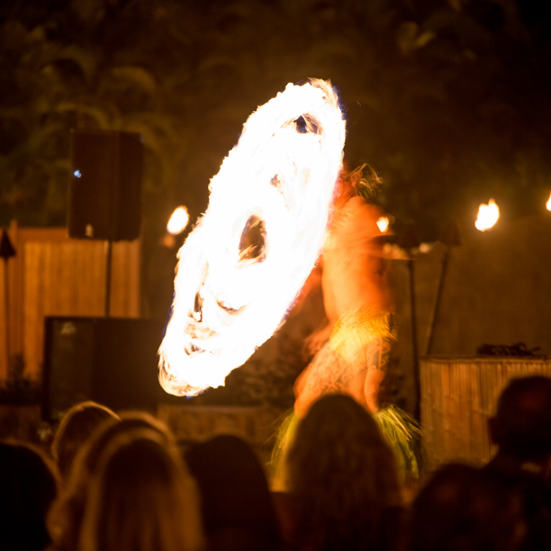 a man stands spinning a fire knife with a dark background for a crowd
