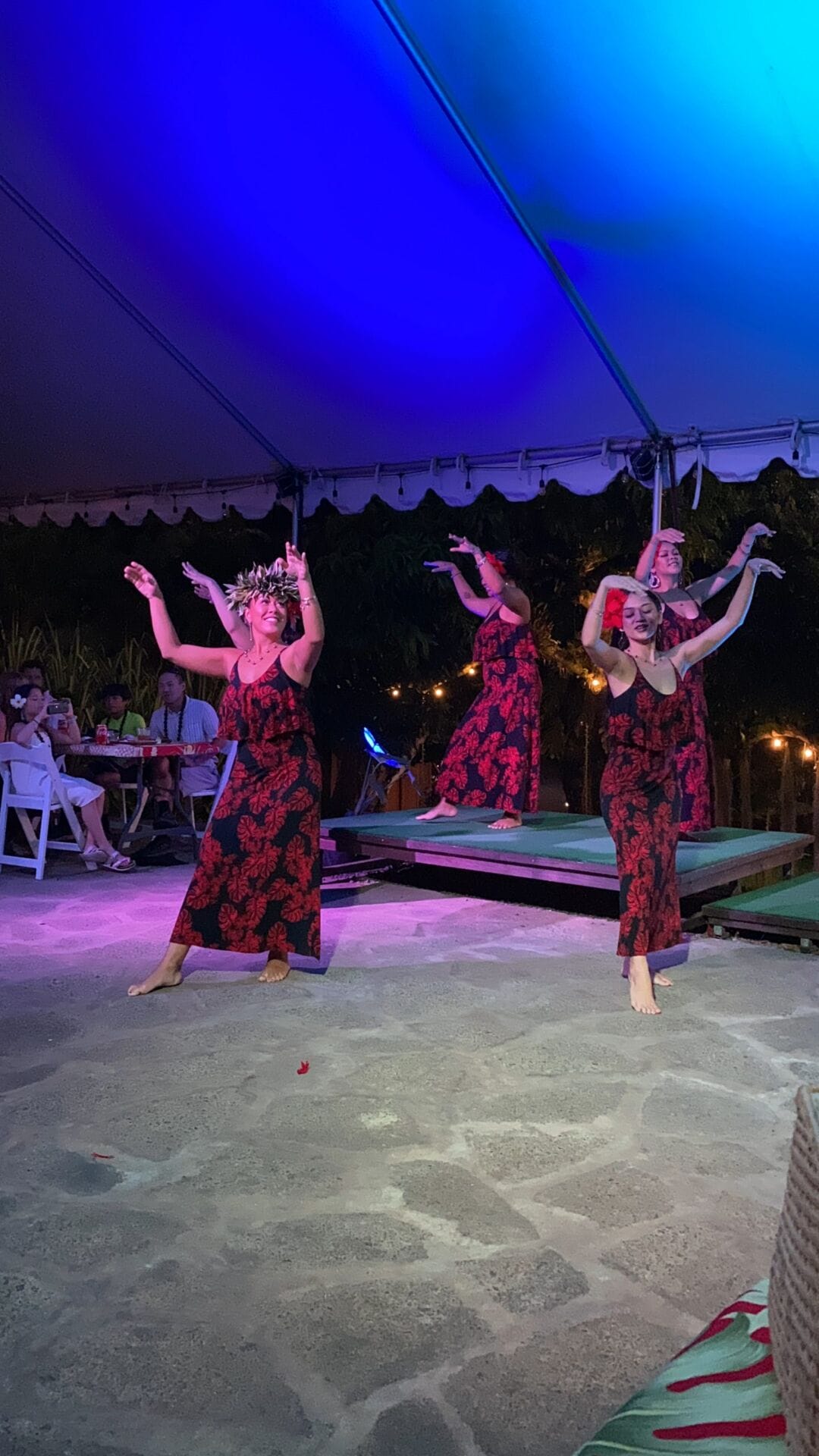 hula dancers in hawaiian luau perform in the evening wearing black and red dresses with flowers in their hair