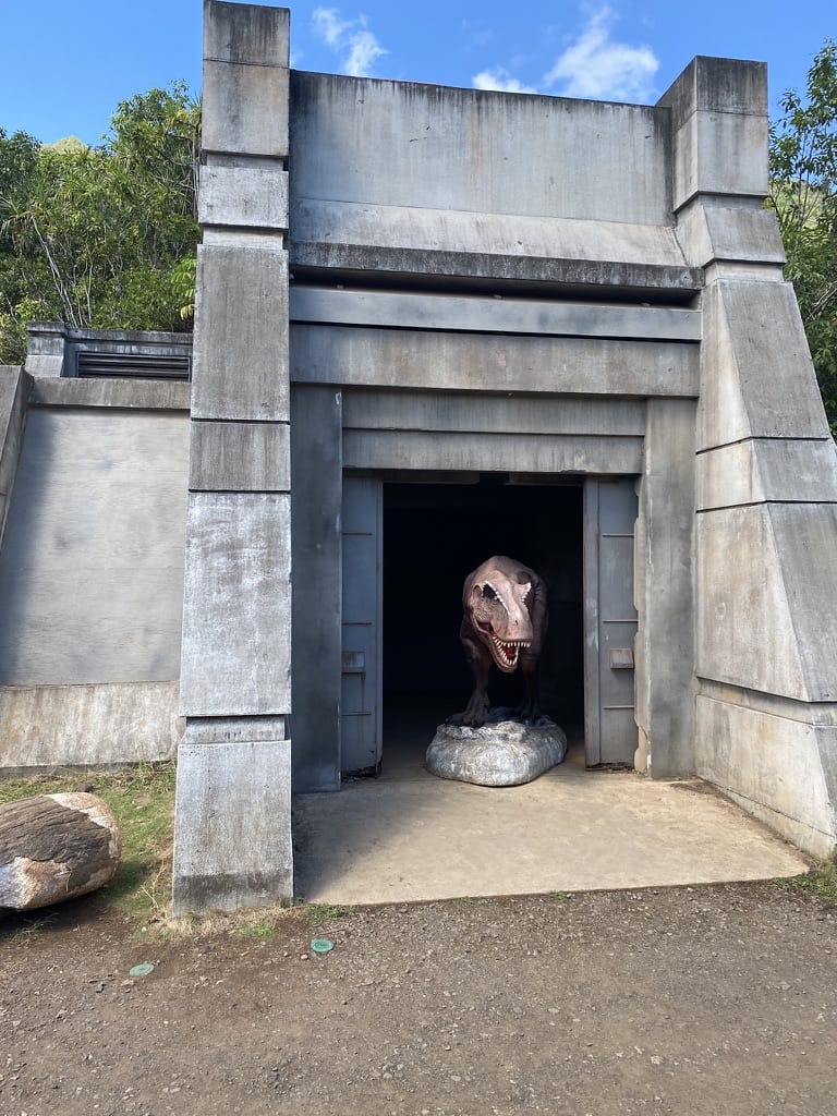 a dinosaur pokes its head out of a cement structure on the kualoa jurassic movie tour
